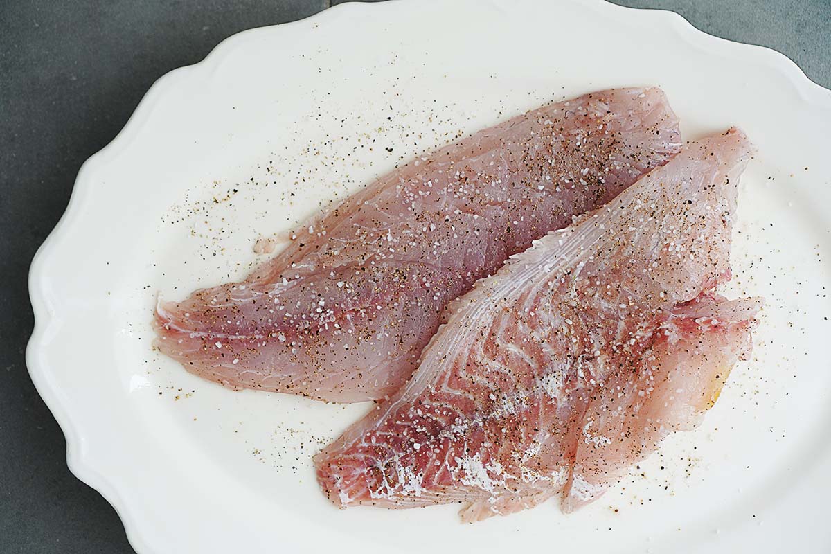 Two large slices of raw fish with salt and pepper placed on a large white plate.