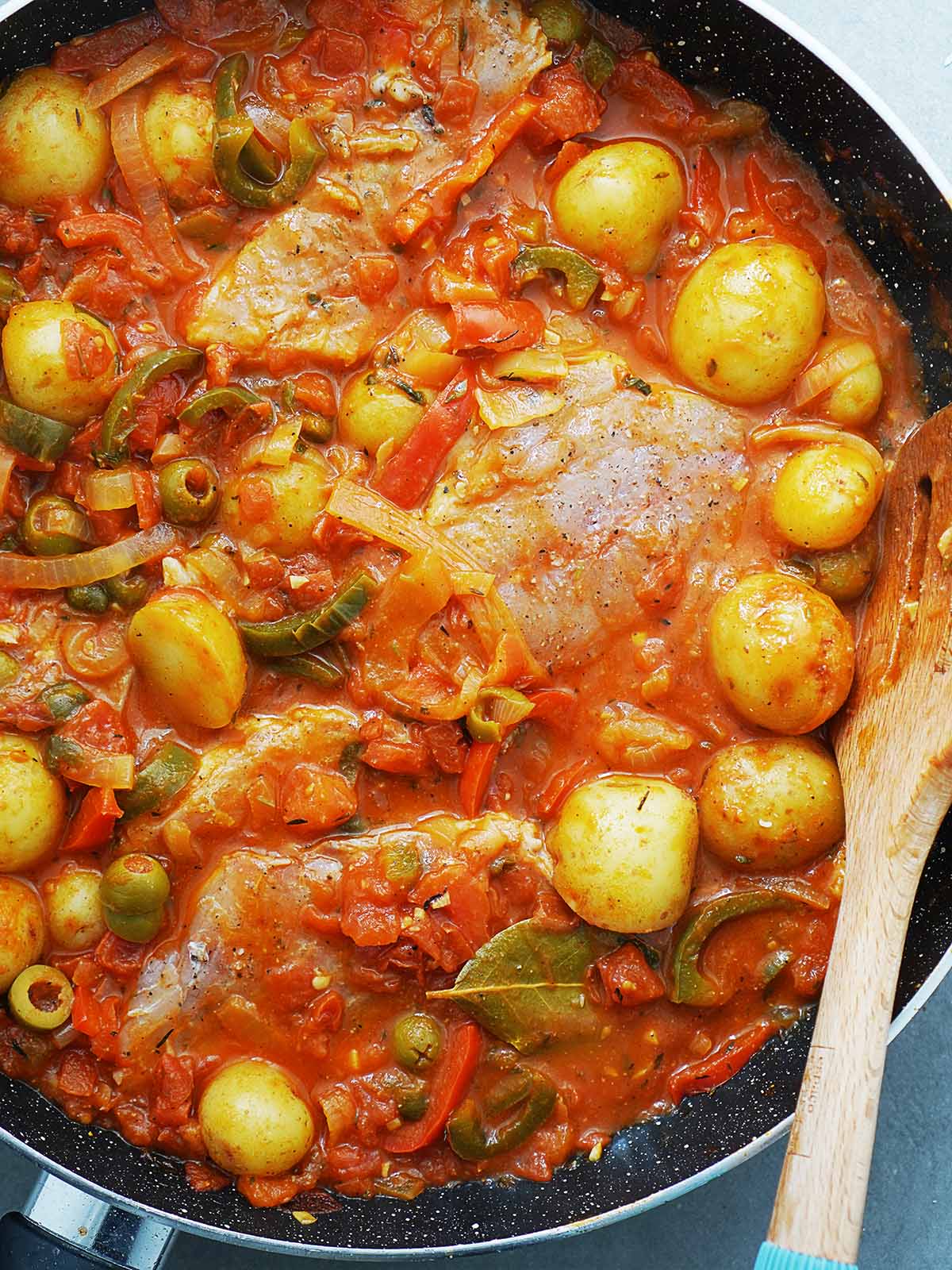 A large skillet with raw fish in the tomato sauce, onions, peppers and potatoes.