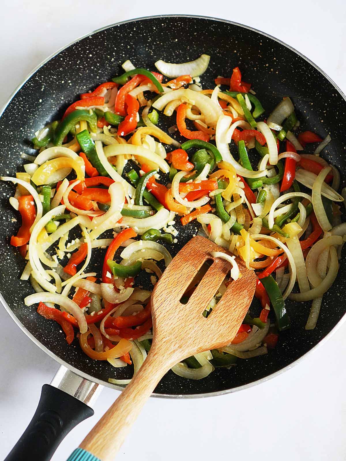 A large skillet sauteing onions and peppers.