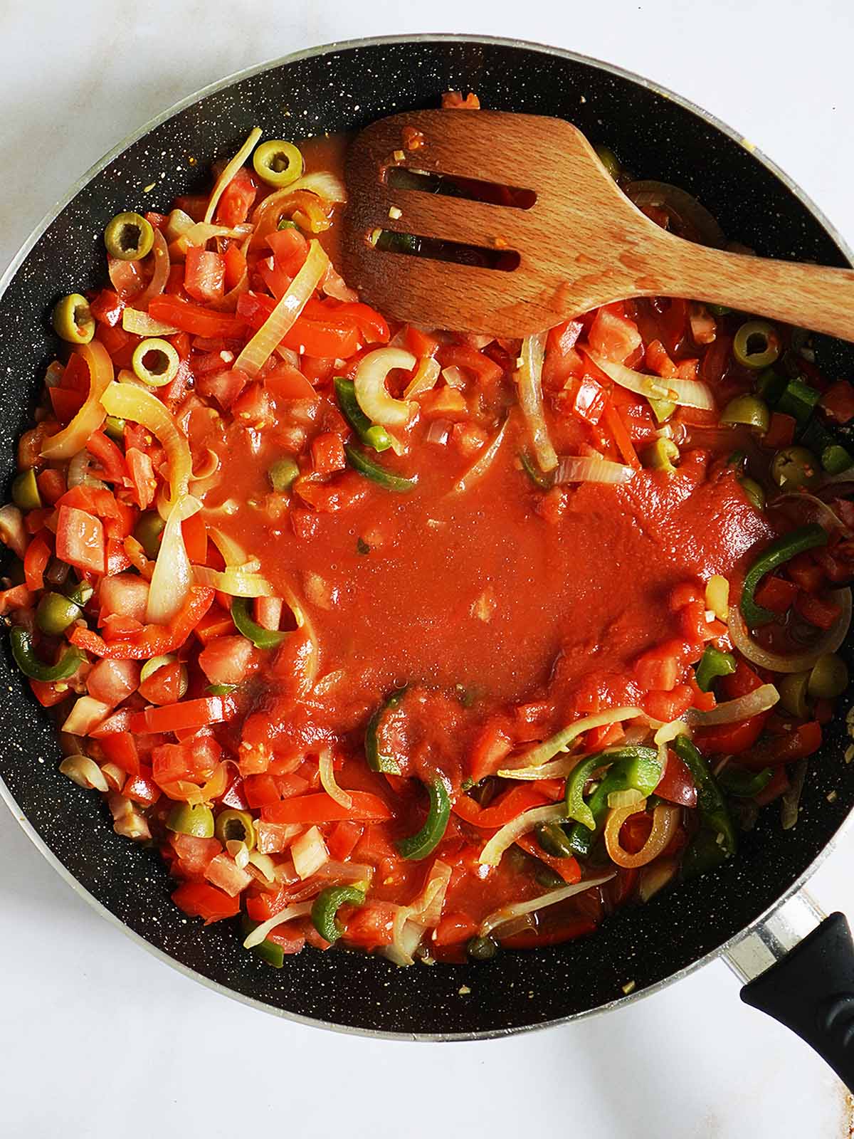 A large skillet with tomato sauce, onions, peppers with a wooden spoon.