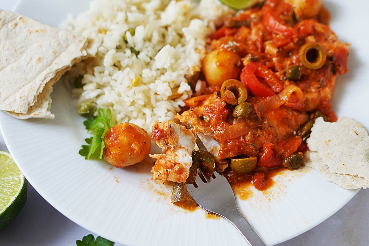 A white dish with Pescado A La Veracruzana covered in sauce and white rice on the side.