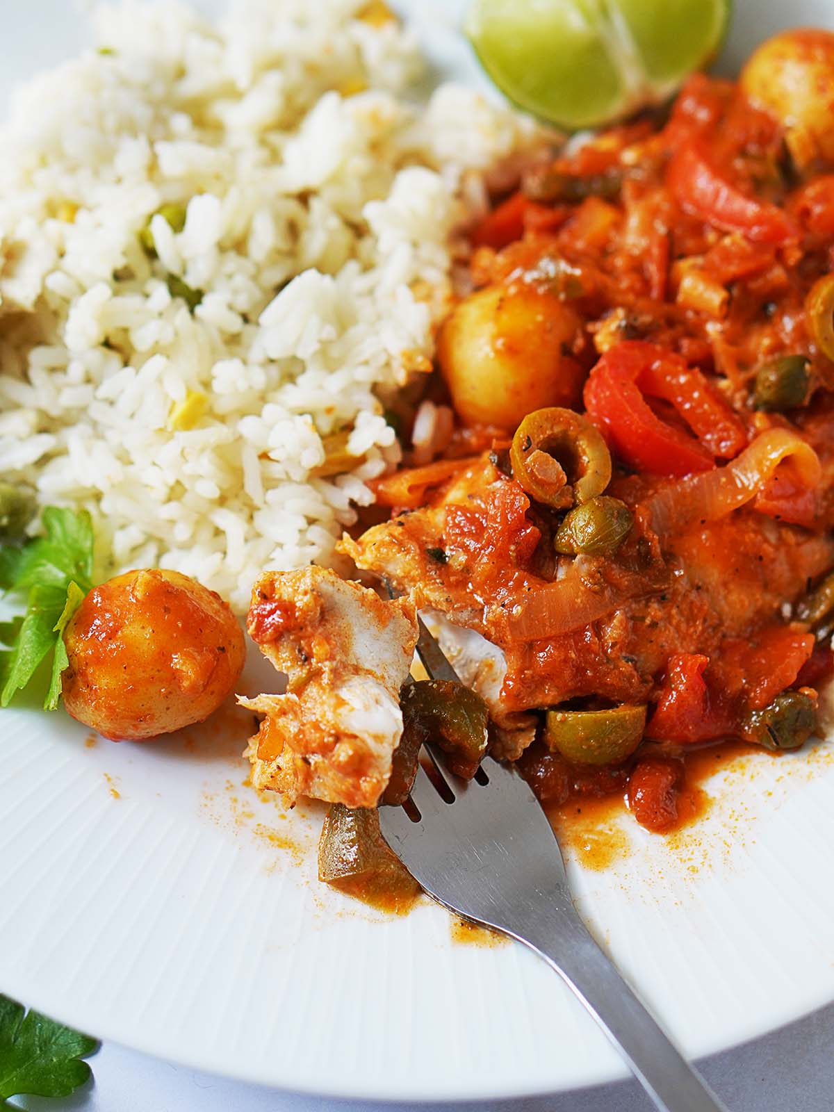 A white dish with the Pescado A La Veracruzana covered in sauce and white rice on the side.