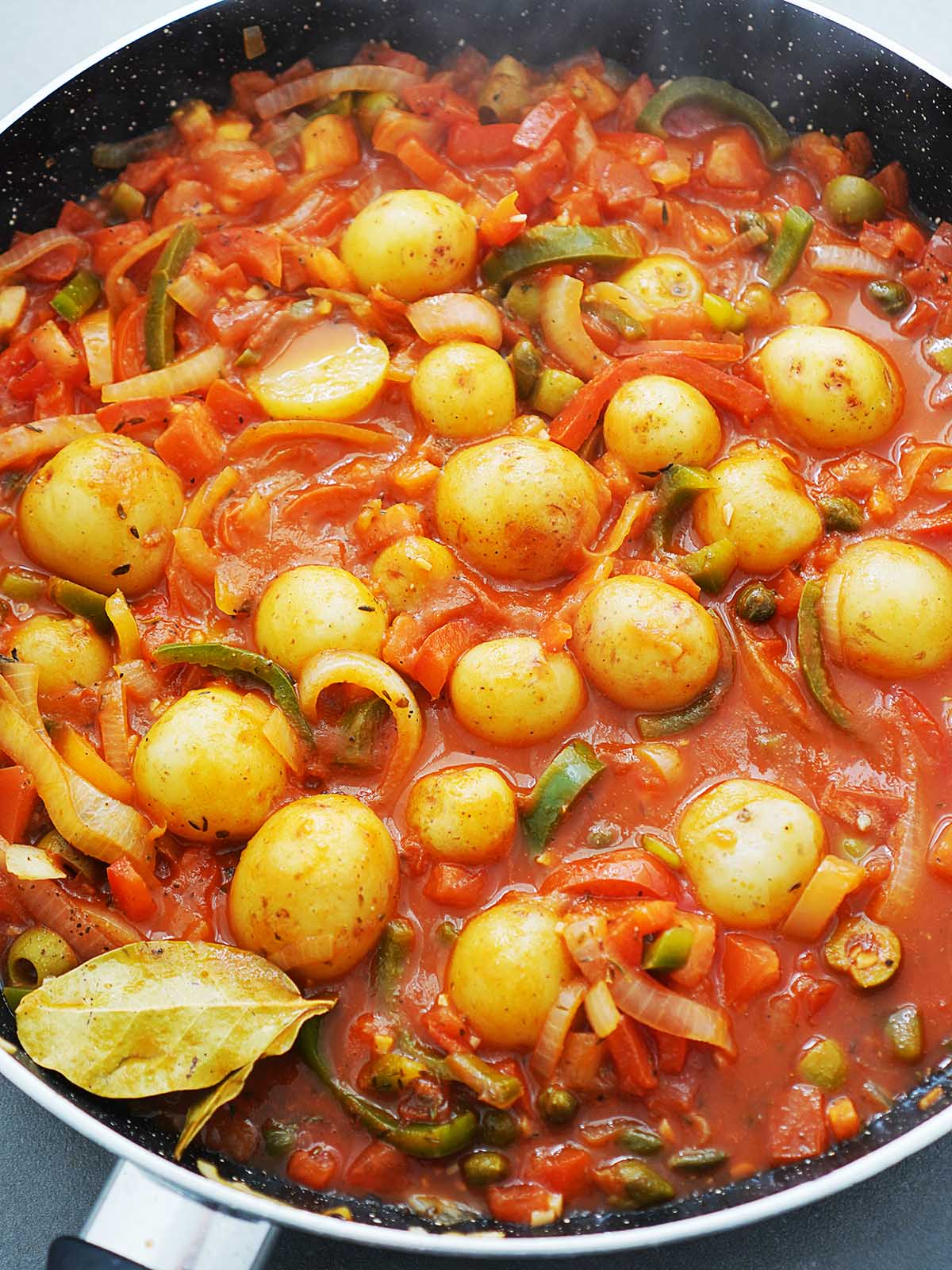 A large skillet with tomato sauce, onions, peppers and potatoes.