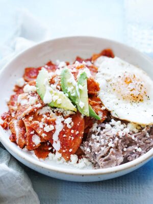 A plate with chilaquiles rojos with a fried egg and beans on the side.