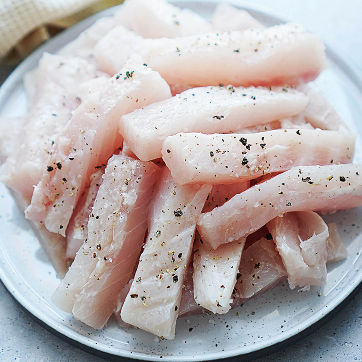 A stack of fish strips on a plate seasoned with salt and pepper.