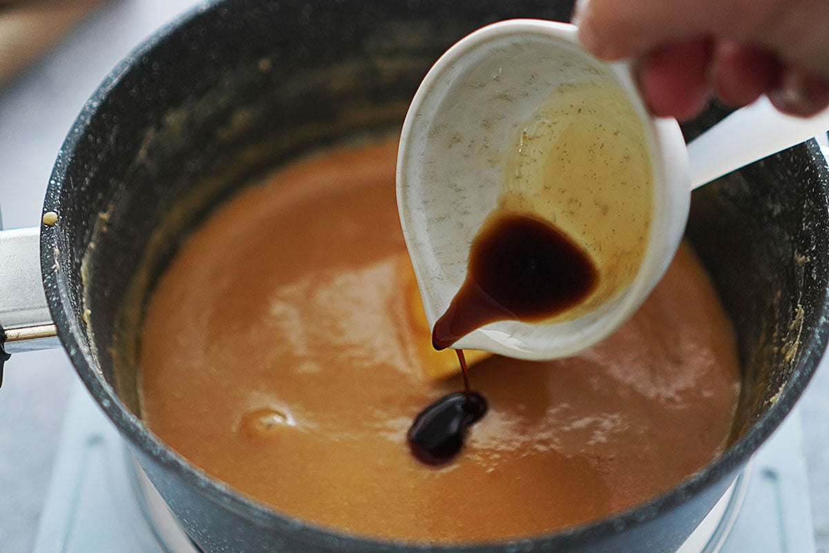 A small pot with caramel sauce and adding vanilla to it.