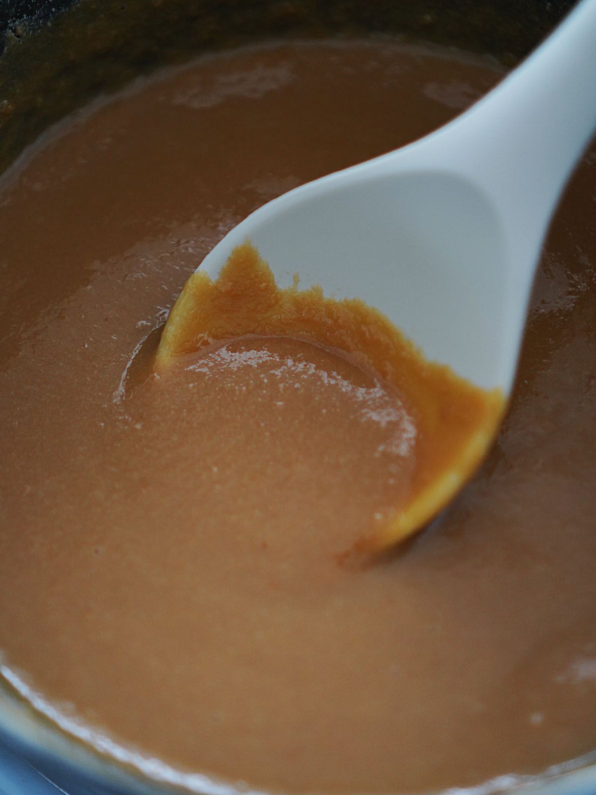 Caramel sauce in a pot with a white spoon.