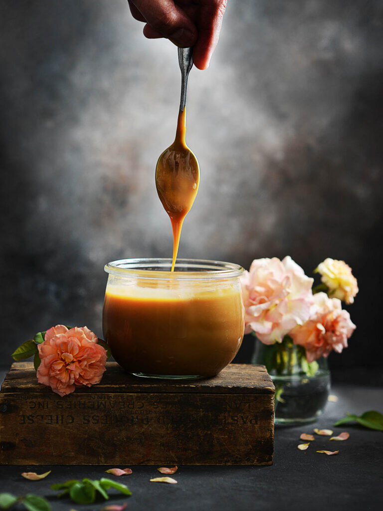 A glass jar with dulce de leche placed on top of a small wooden box.