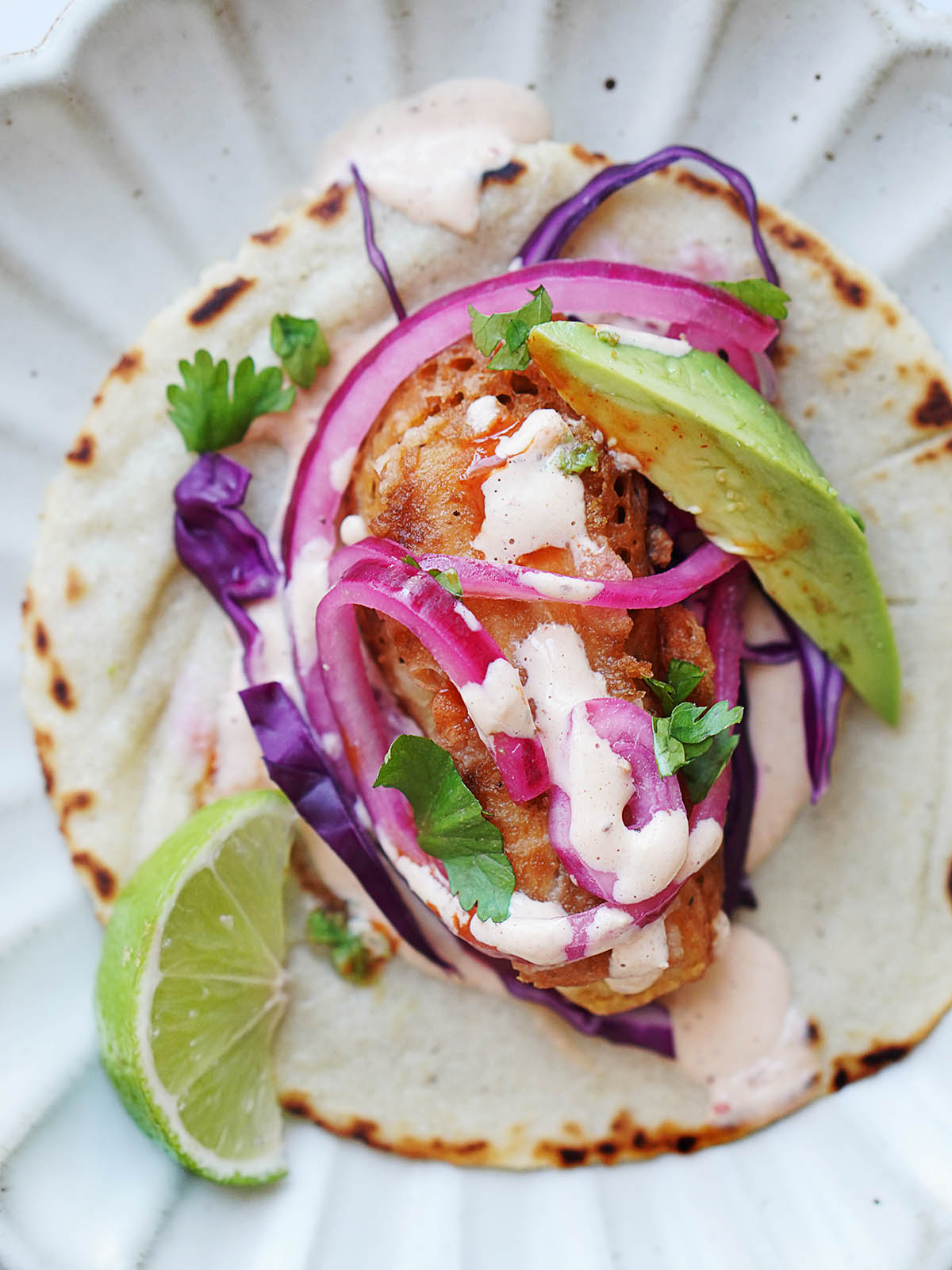 A baja fish taco topped with onions, cabbage and chipotle crema. A slice of lime on the side.