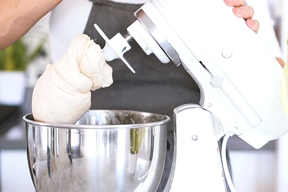 A white mixer with dough on the hook tool.
