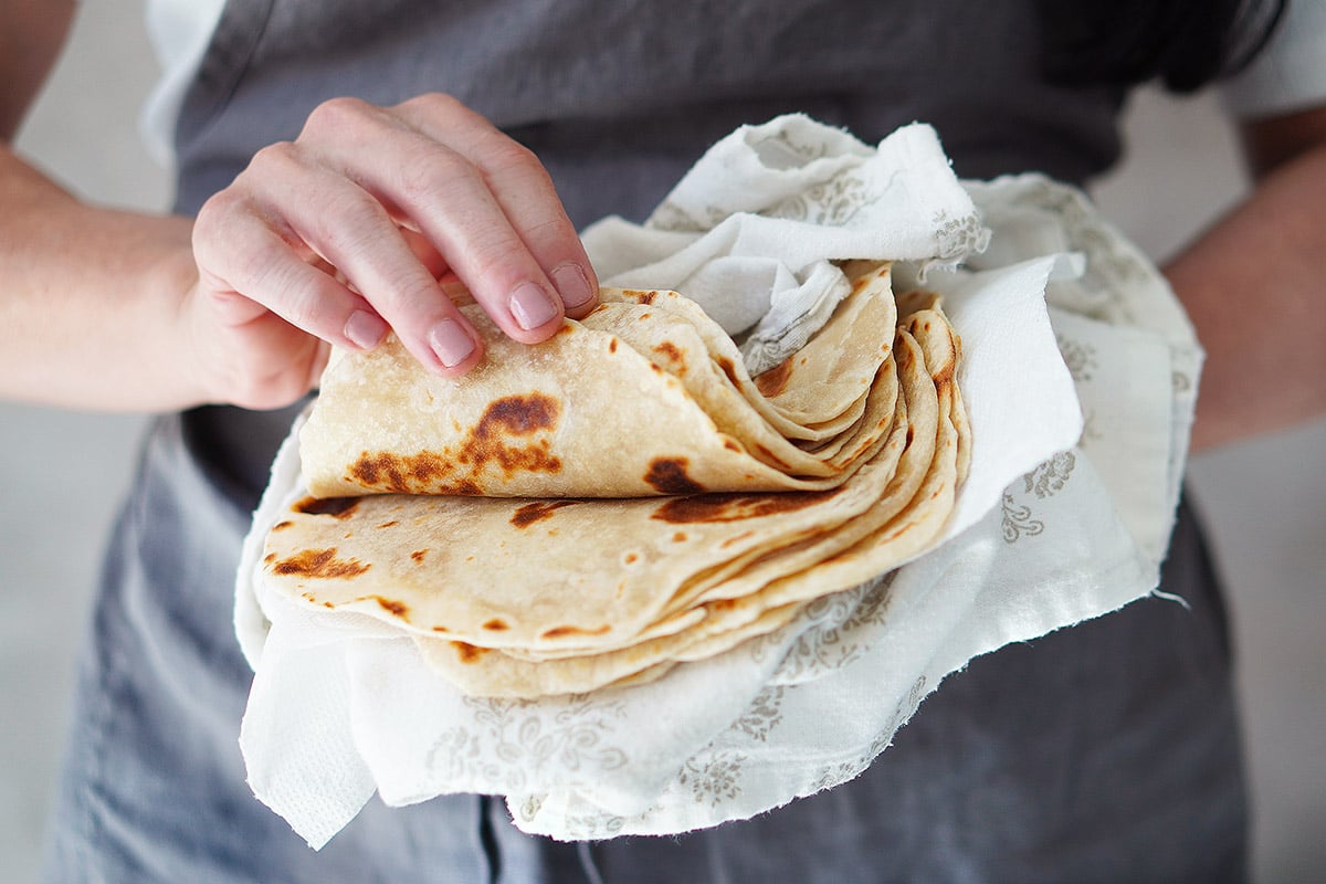 Two hands hold a stack of homemade tortillas.