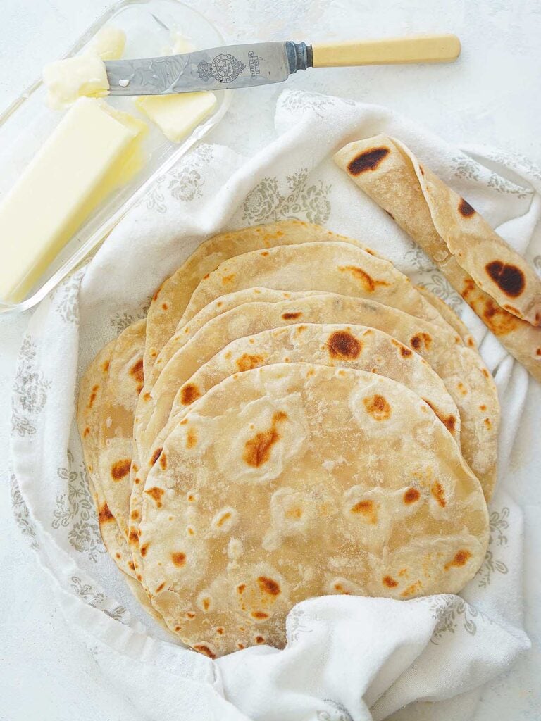 A stack of flour tortillas placed inside a kitchen towel.