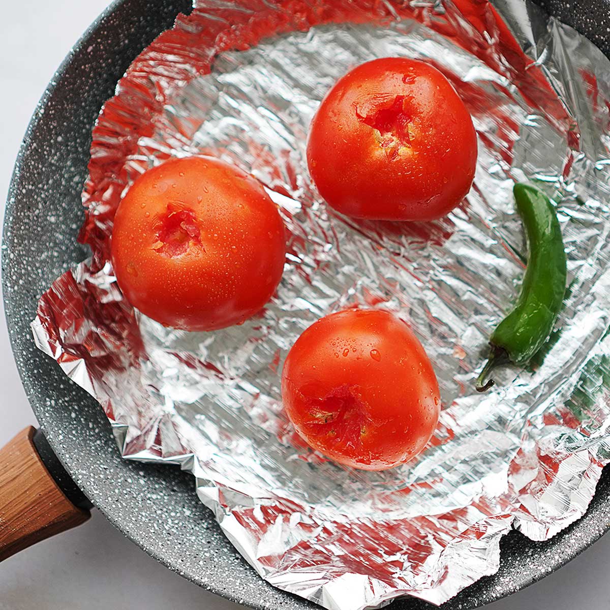 A skillet with tomatoes lined with aluminum foil.