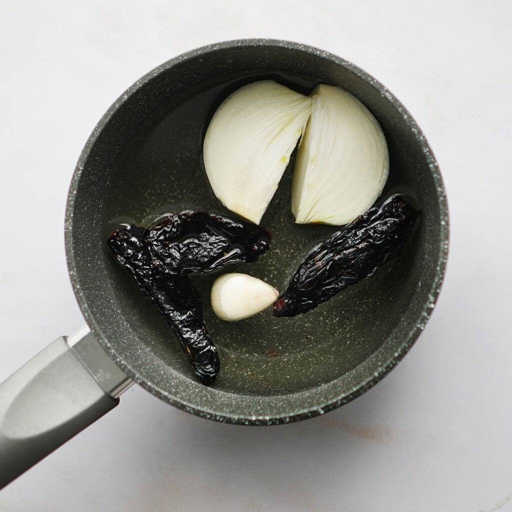 A small saucepan with chile moritas, garlic clove and onion.