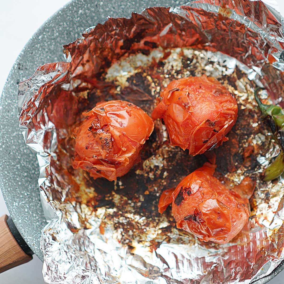 3 roasted tomatoes on a skillet lined with aluminum foil.
