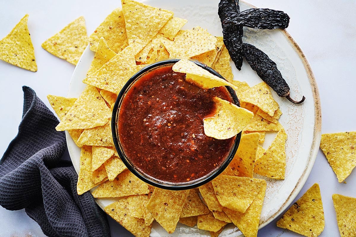 A bowl of salsa morita with tortilla chips on the side and two morita chiles on the side.