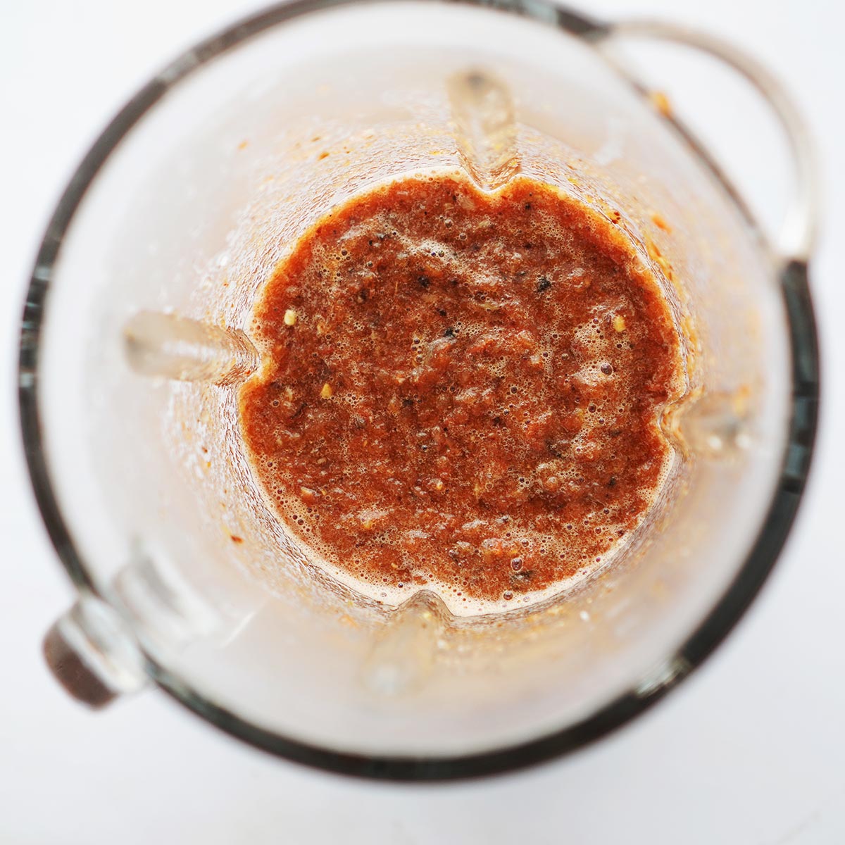 A blender glass with blended red salsa.