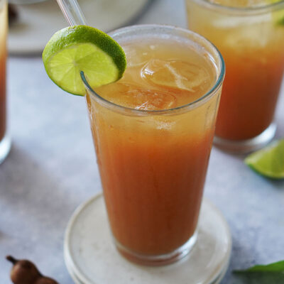 A single glass filled with ice and agua de tamarindo garnished with a slice of lime and a glass straw.