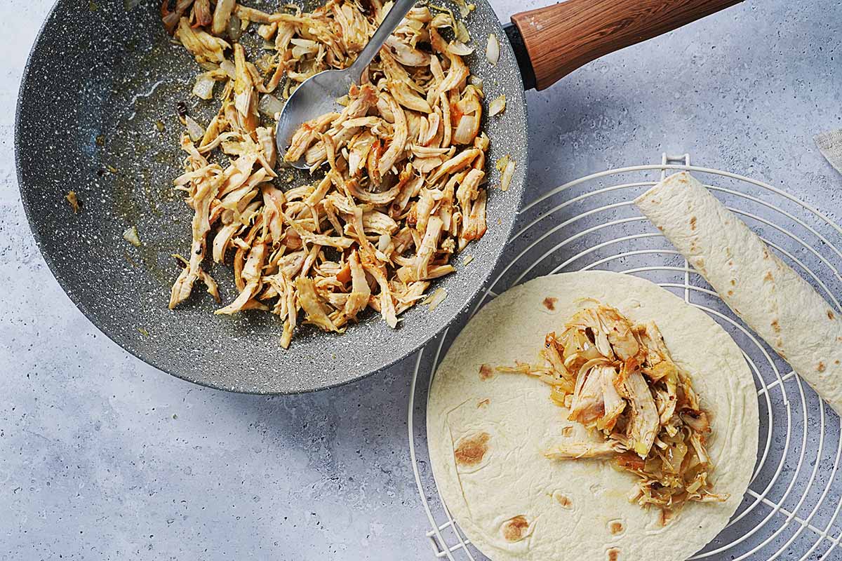 Filling a flour tortilla with shredded chicken.