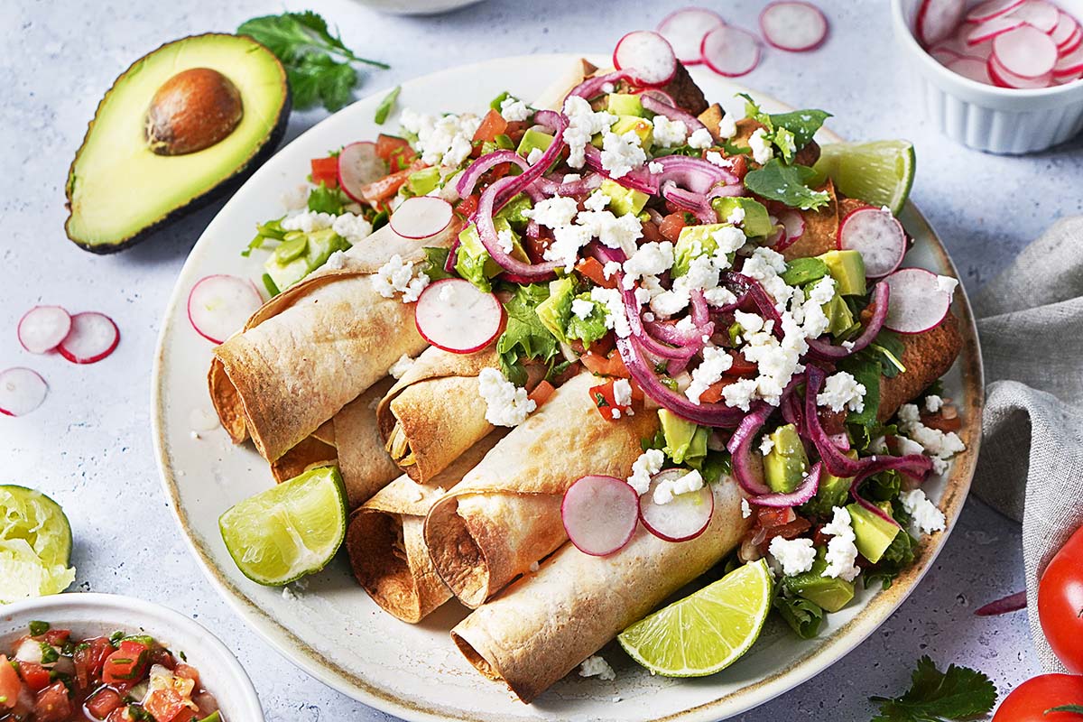 A plate with 7 chicken flautas topped with avocado, lettuce, pickled onions and radishes.