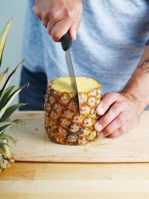 A man's how to slice a fresh pineapple in the middle.