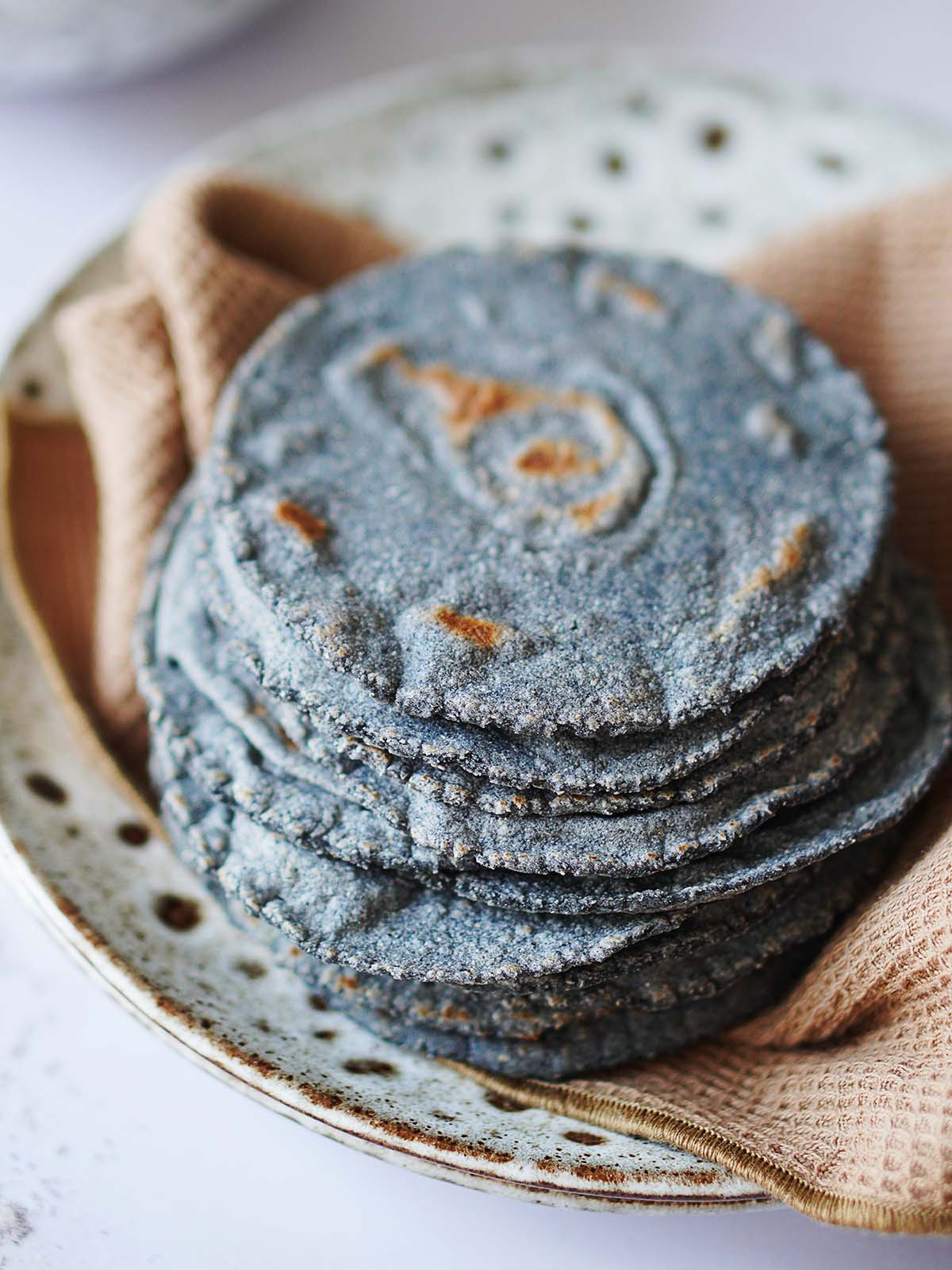 A stack of blue corn tortillas placed on a brown kitchen towel.