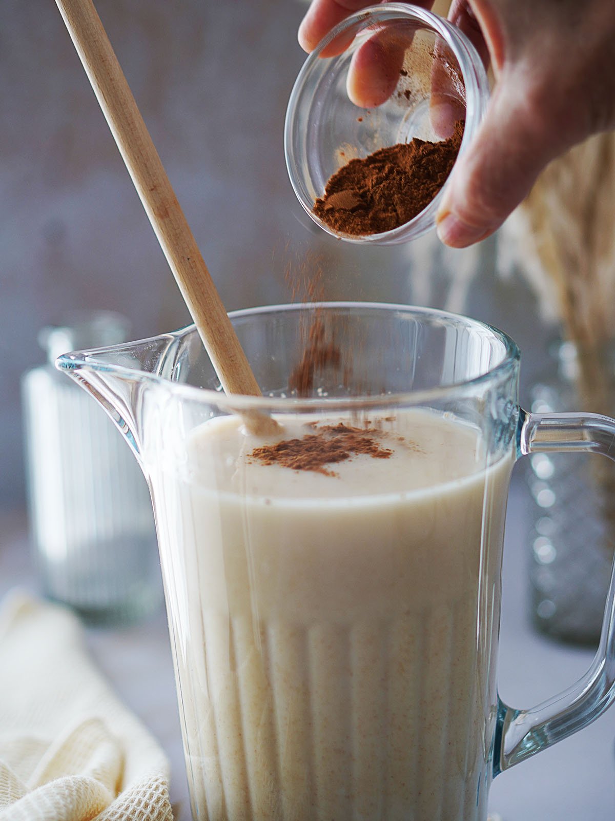 Adding cinnamon to a jar filled with a milky drink.
