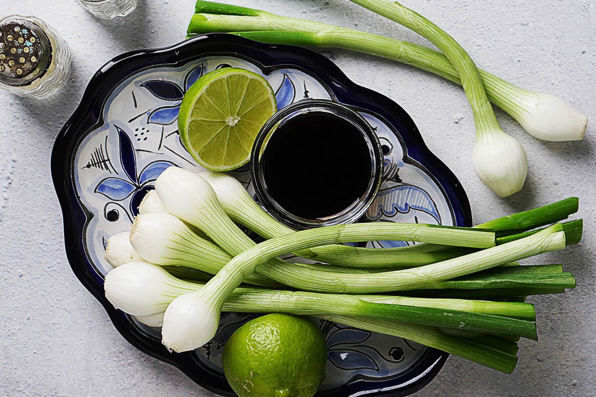 Raw green onions on a blue plate with soy sauce and a lime on the side.