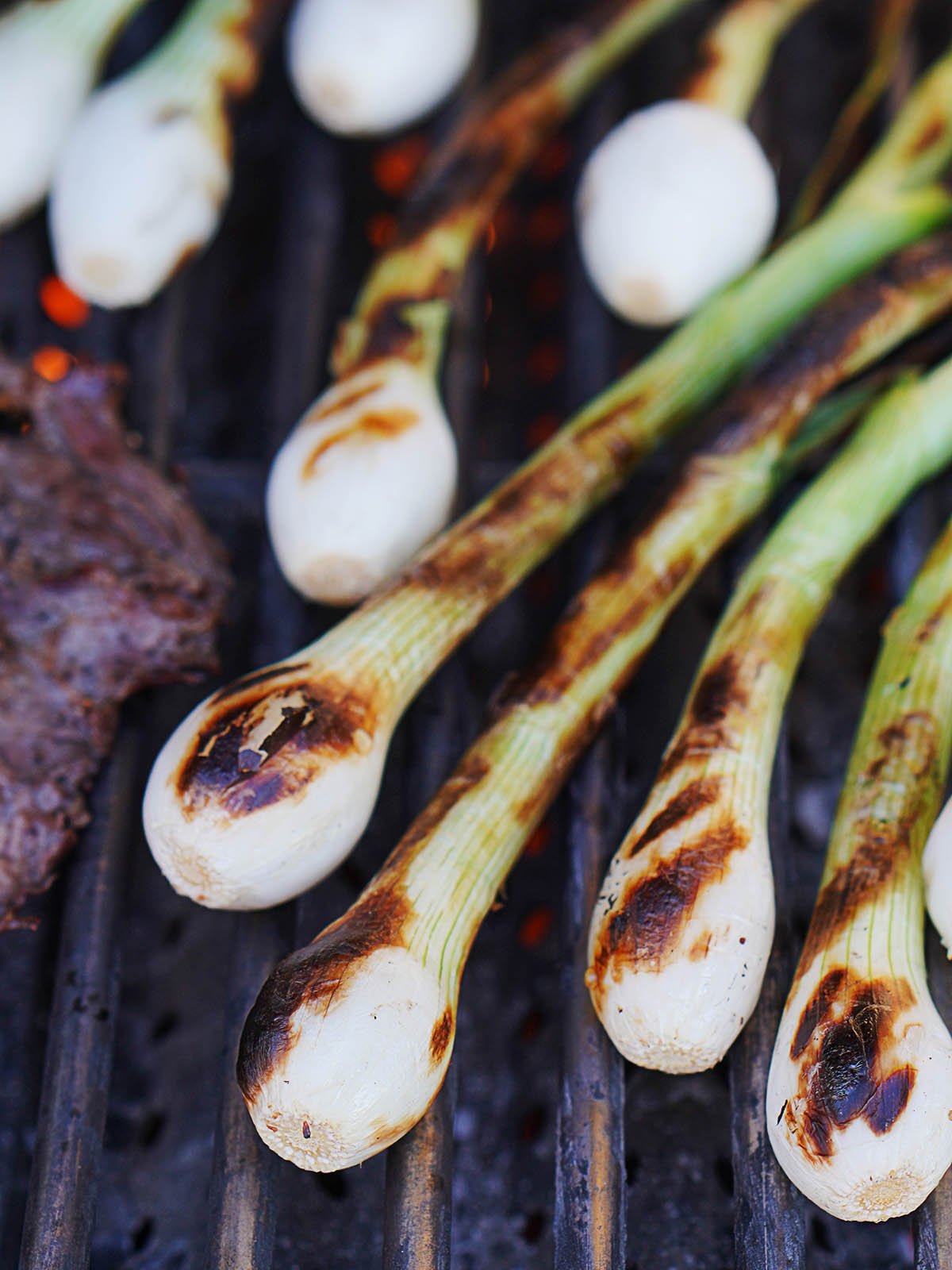 Green onions on a grill with carne asada on the side.