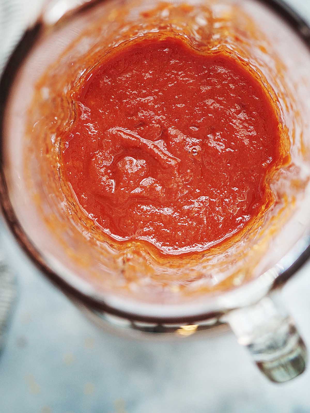A blender glass with blended red sauce.