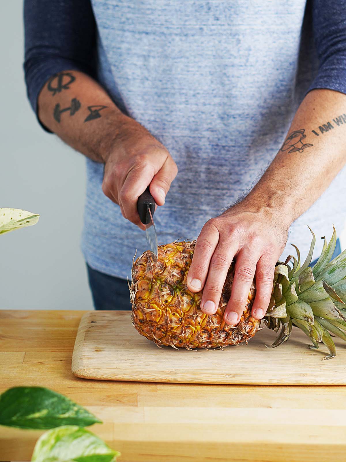 A man showing how to slice a pineapple with a knife on a cutting board.