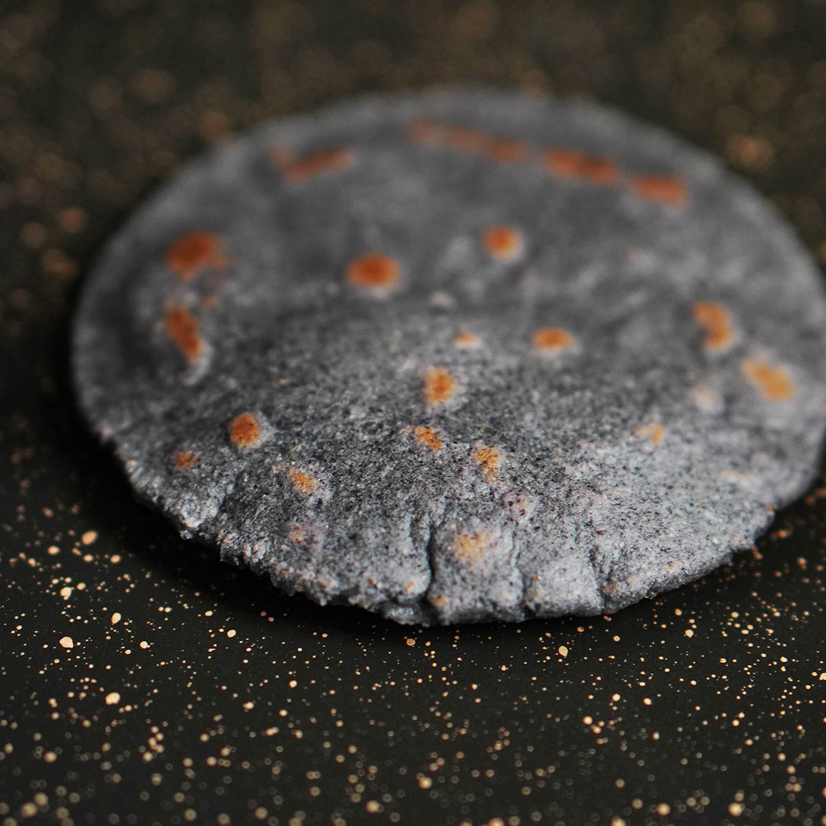 A blue corn tortilla cooked on a black skillet with brown marks.