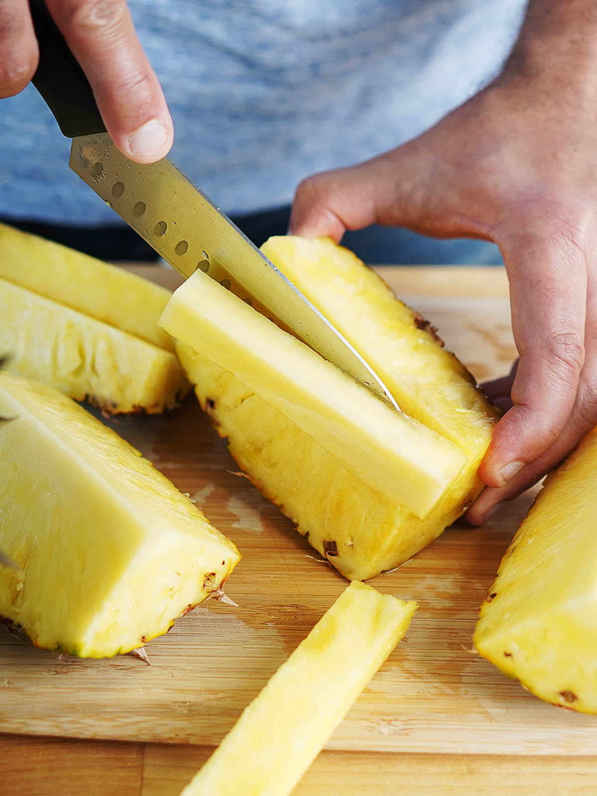A hand showing how to remove the core of a pineapple with a knife.