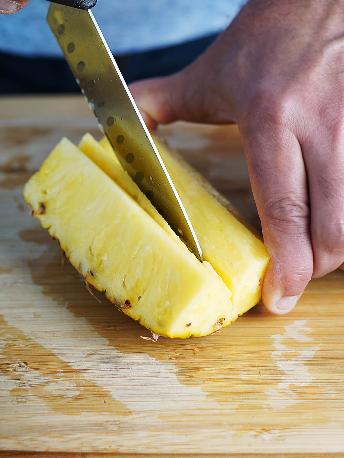 A hand removing the core of a pineapple with a knife.