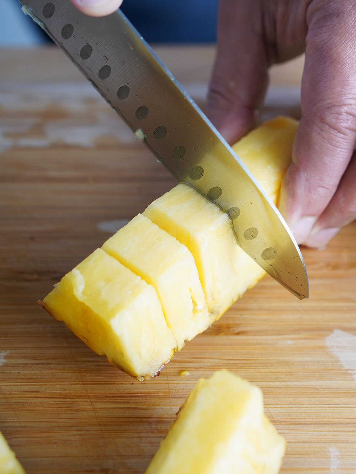 A hand holding a knife cutting thru pineapple slices.