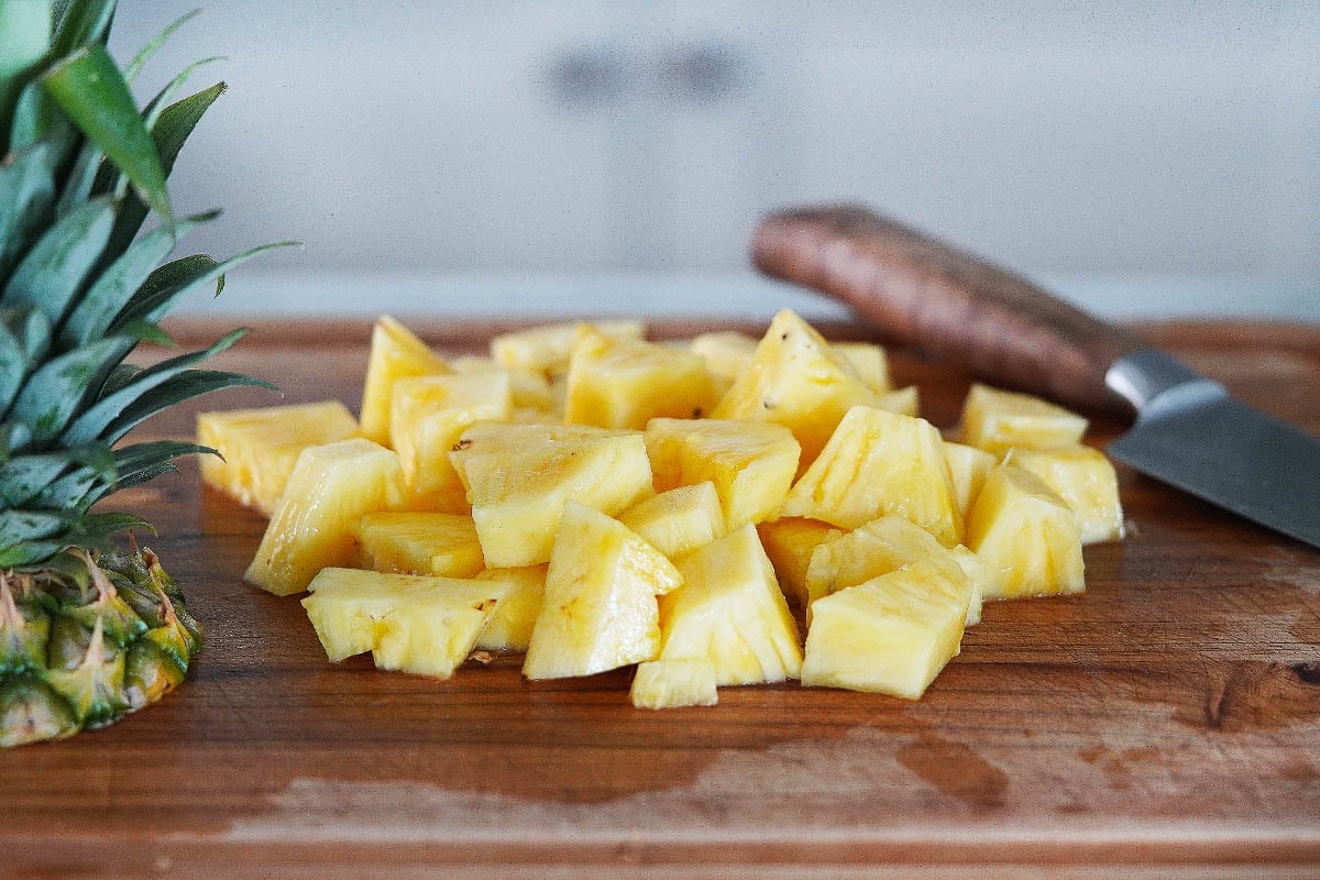 Pineapple chunks on a cutting board with a knife on the side.