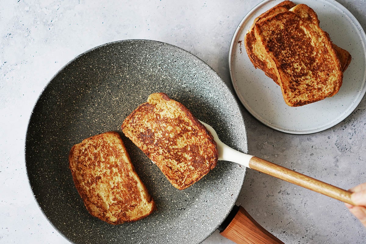 Toasting two slices of bread in a gray skillet and a white spatula flipping one bread.