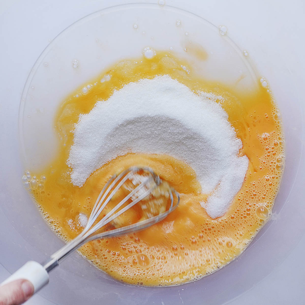 Whipping eggs and sugar with a whisk in a large bowl.