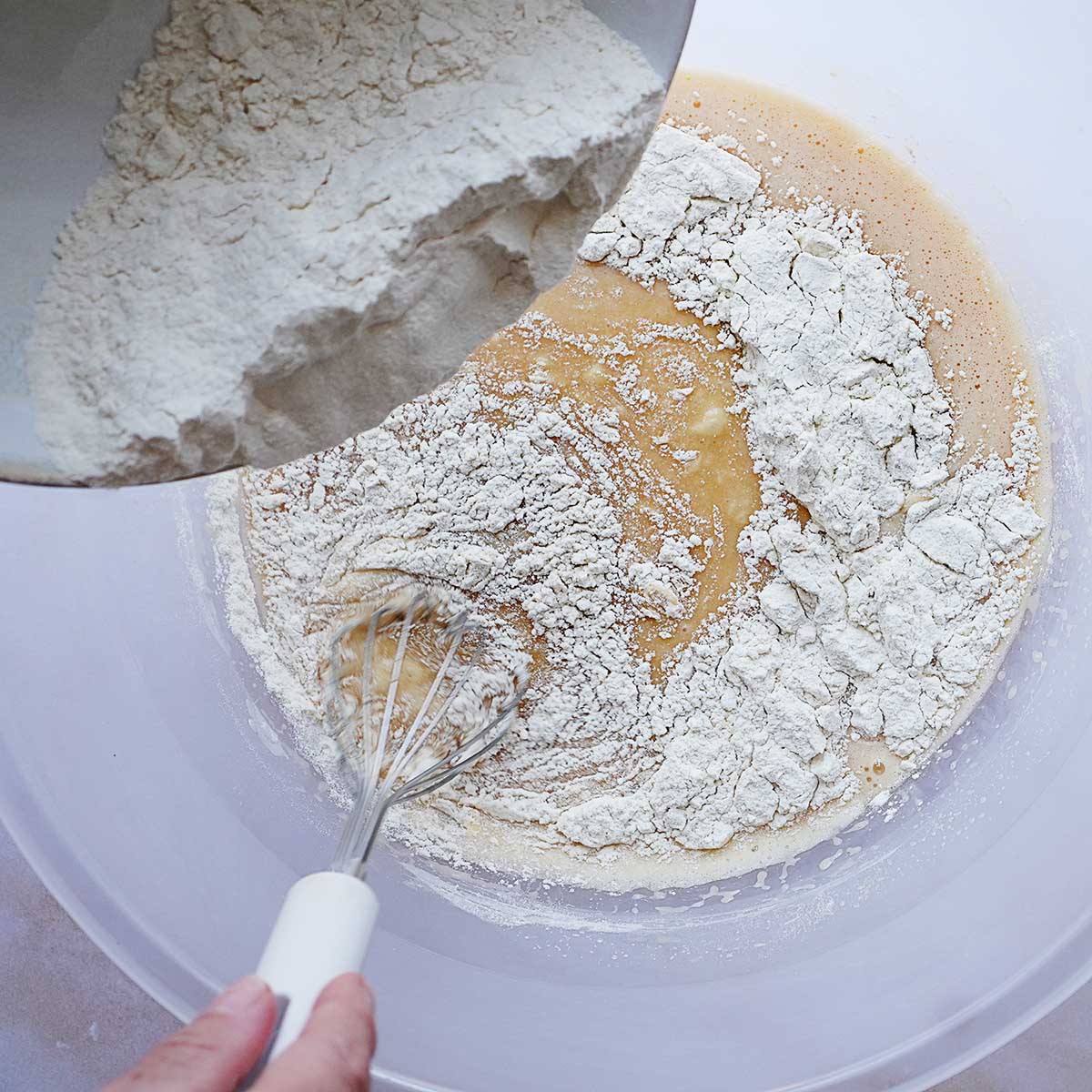 Adding flour from a bowl into a large bowl with an egg mixture.
