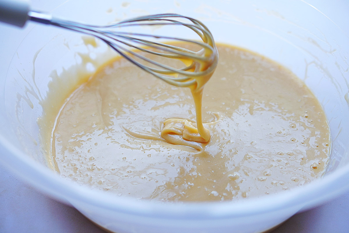A whisk in a white bowl with batter.