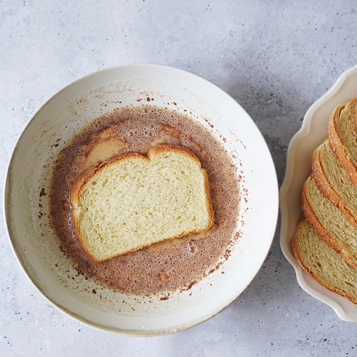 A slice of bread dipped in an egg, milk with cinnamon mixture on a large bowl.