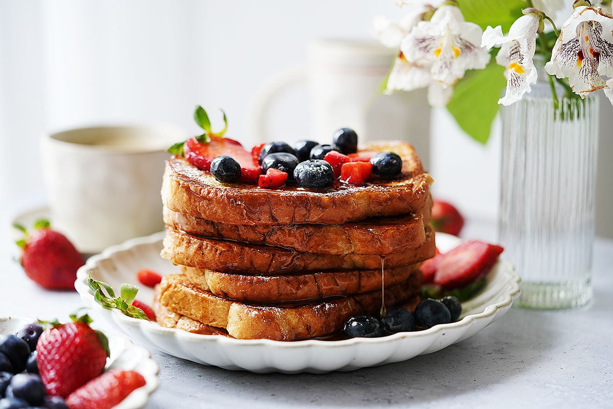 A stack of Pan Frances slices on a white plate topped with blueberries and strawberries.