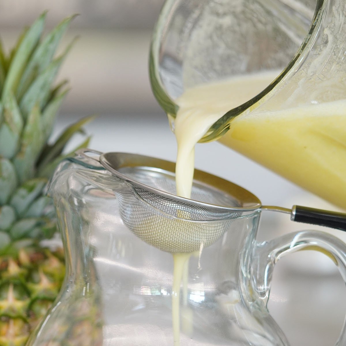 Pouring the pineapple water thru a small strainer into a jar.