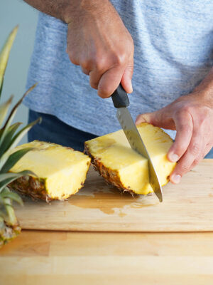 A hand with a knife cutting a fresh pineapple in fourths.