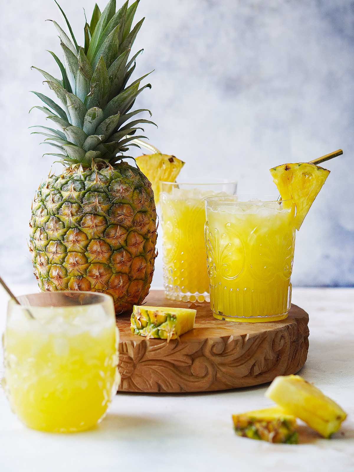 Three glasses with agua de piña and a whole pineapple next to them.