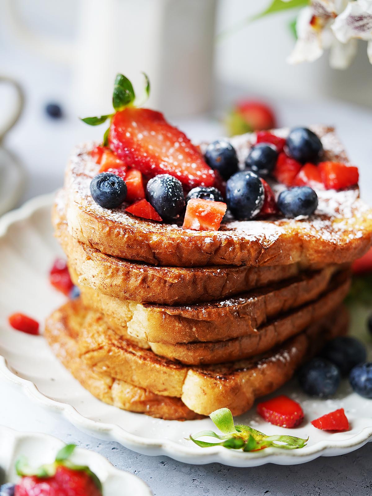 A stack of toast slices on a white plate topped with blueberries and strawberries.