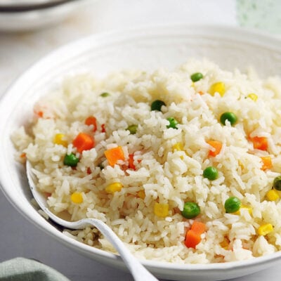A white bowl with Arroz Primavera with a white spoon in it.