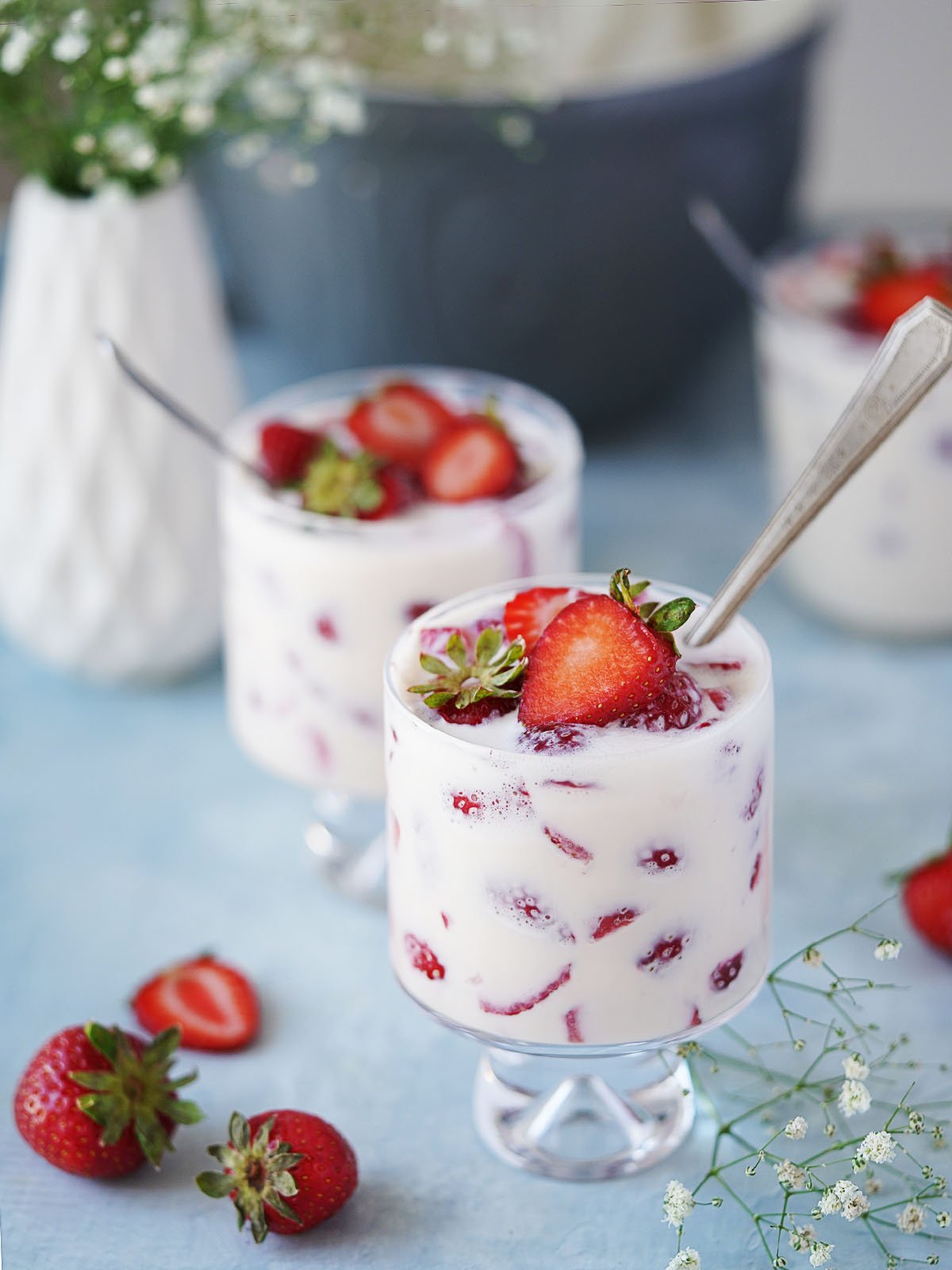 Three small glasses with strawberries and cream and a spoon.