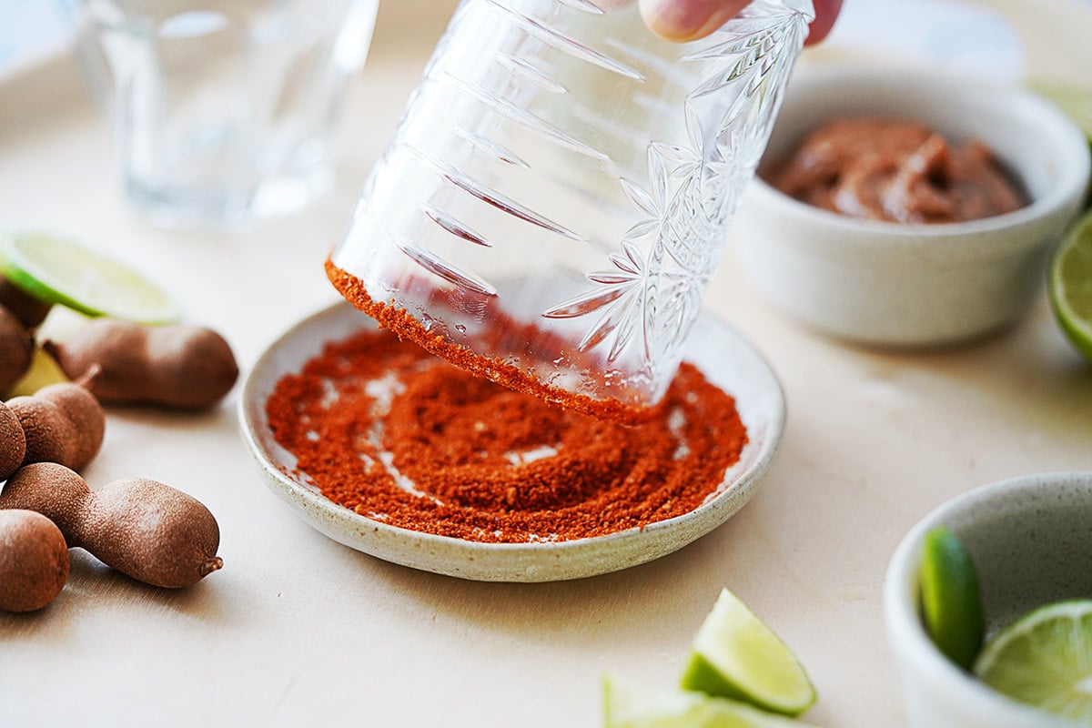 Dipping the edge of a cocktail glass into a small plate with chili powder.