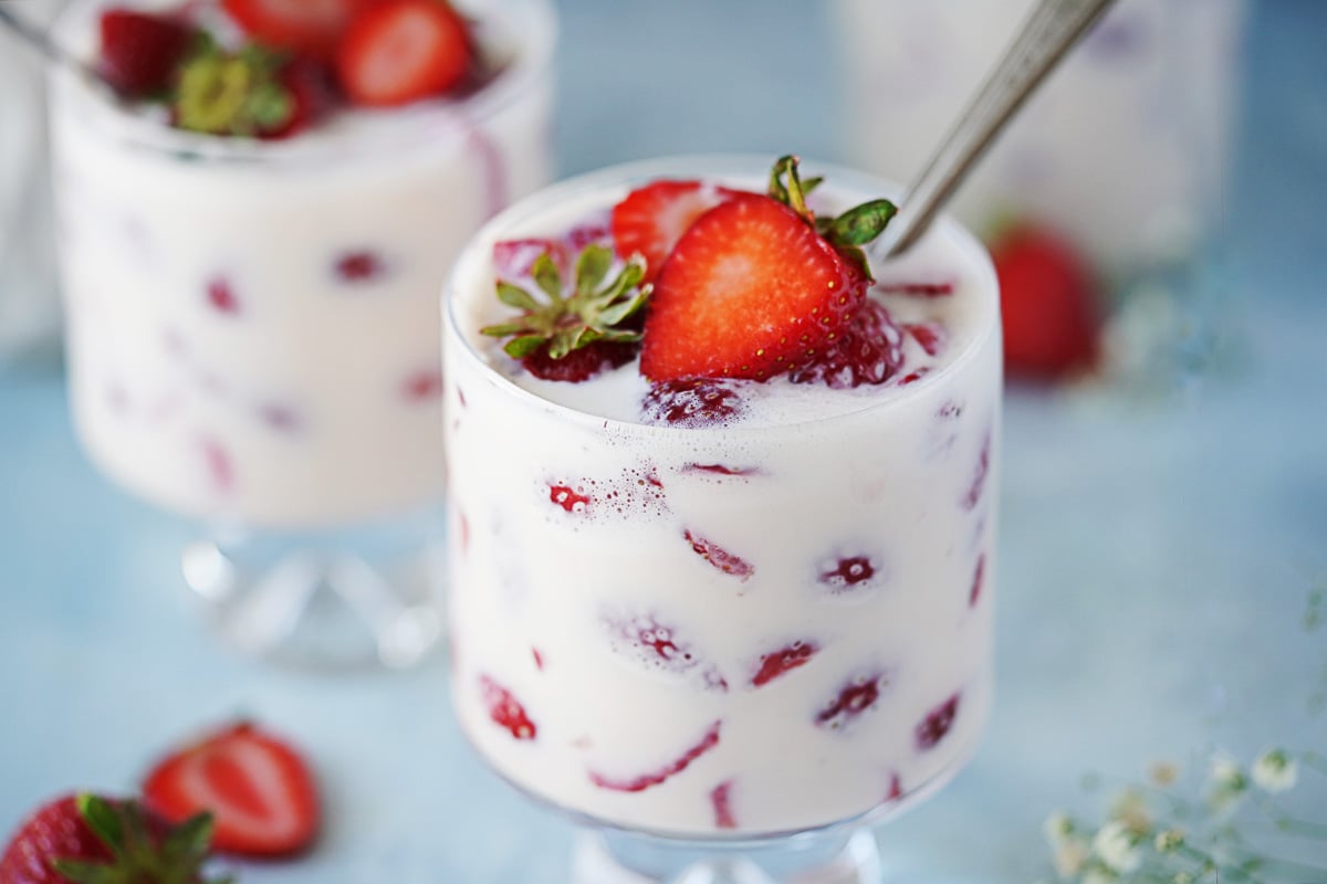 Three small glasses with fresas con crema topped with a fresh strawberry.